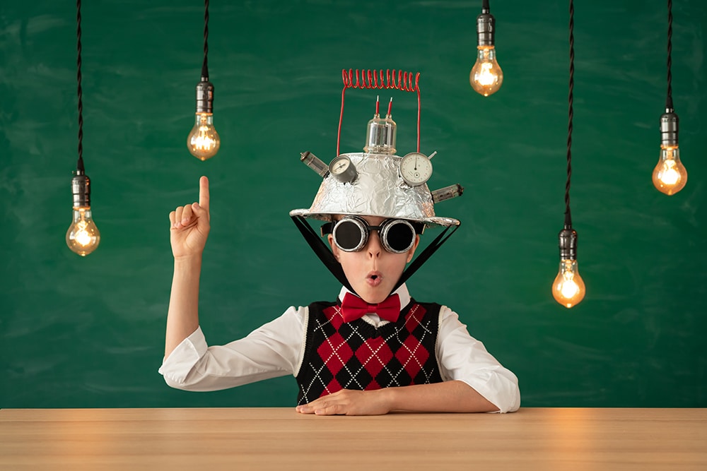 Happy child in classroom. Funny kid with light bulb against green chalkboard background. Innovation technology in education. Bright new idea concept. Back to school